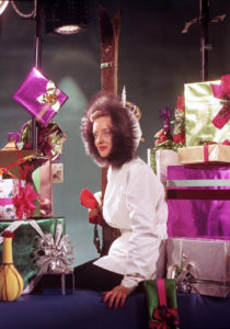 Bette Davis surrounded by gifts and dressed for the chilly Hollywood weather in a Christmas photo.